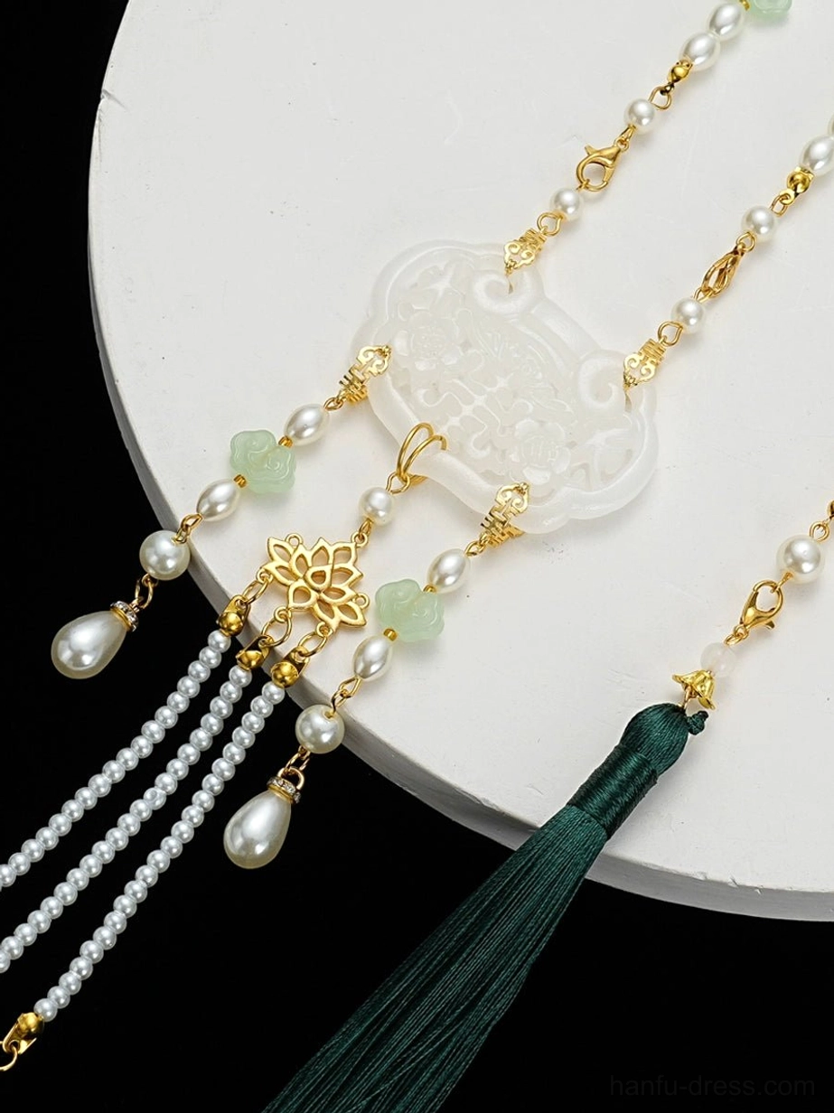 Close-up of Chinese tassel necklace centerpiece showing white longevity lock, gold floral detail, teardrop pearl-like pendants, layered tassels, and dark green hanging tassel