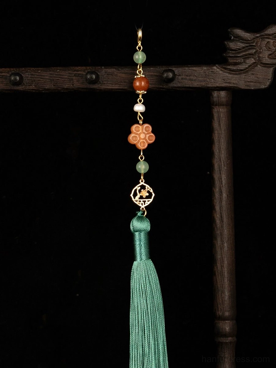 Close-up of a standalone Chinese tassel pendant accessory with a flower-shaped decorative charm, openwork gold-tone ornament, and long green silk tassel