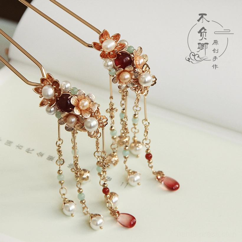 Chinese traditional hair stick with warm gold metal details decorative pearls red beads and hanging tassels shown from an overhead view