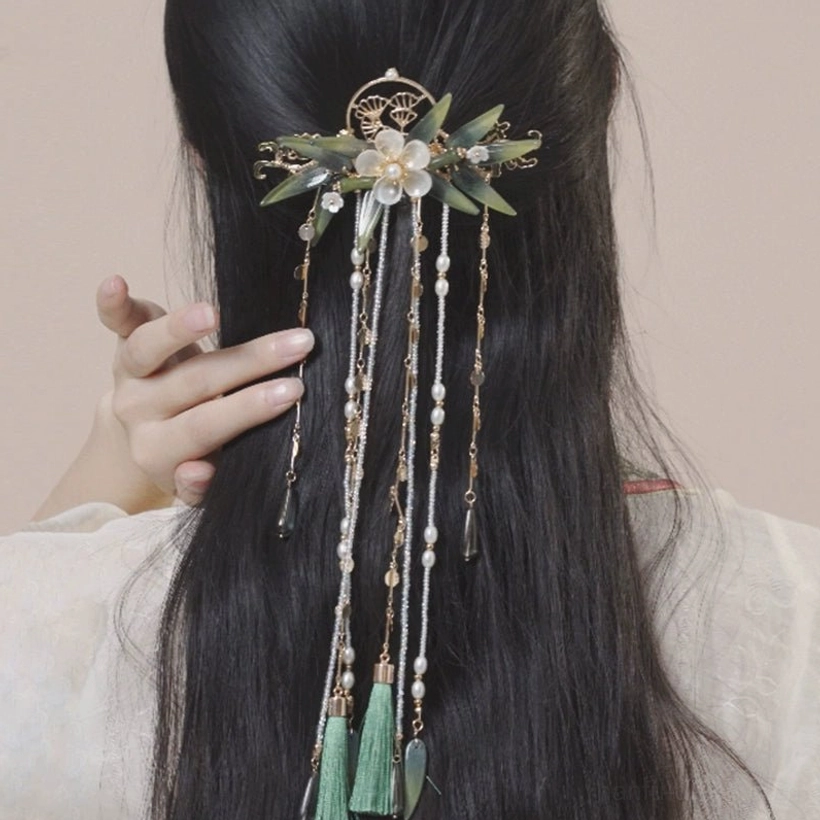 Back view of a model touching her hairstyle while wearing a Chinese vintage tassel hairpin with floral ornaments, green bamboo details, and layered bead strands