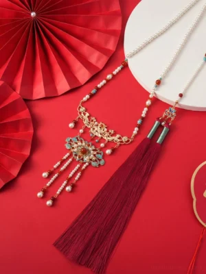 Top view of Chinese wedding Hanfu necklace with layered gold tone chains floral cloisonne pendants red beads pearl accents and dark red tassel
