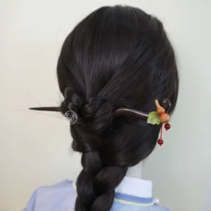 Medium back view of a Chinese wooden hair stick in braided black hair, decorated with a green leaf accent, wooden gourd ornament, and double red bead tassel