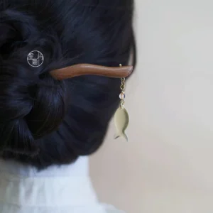 Traditional Chinese wooden hair stick with translucent fish pendant securing a dark low bun in a Hanfu-inspired hairstyle