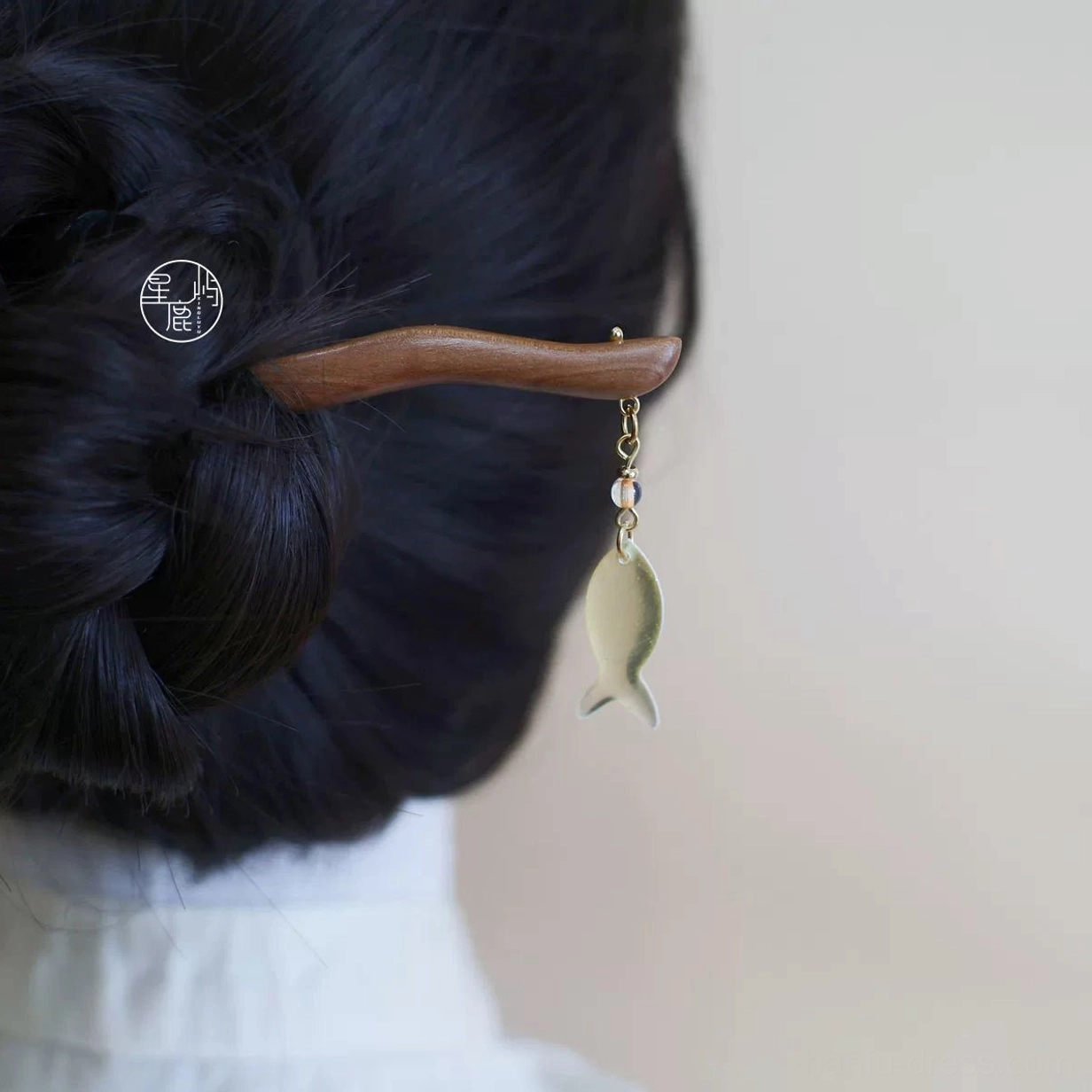 Traditional Chinese wooden hair stick with translucent fish pendant securing a dark low bun in a Hanfu-inspired hairstyle