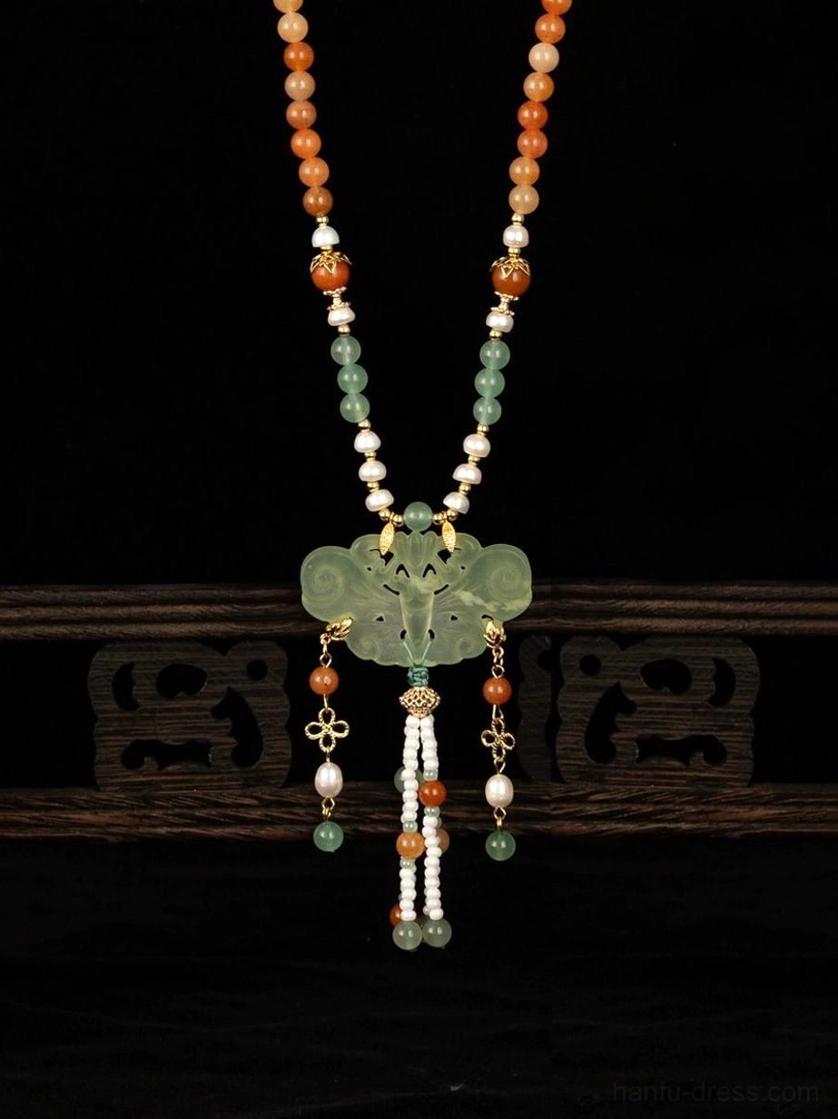 Front close-up of a Chinese yingluo necklace with a large cloud-shaped green ornamental pendant, mixed beads, pearl details, and layered tassel charms on a wooden stand