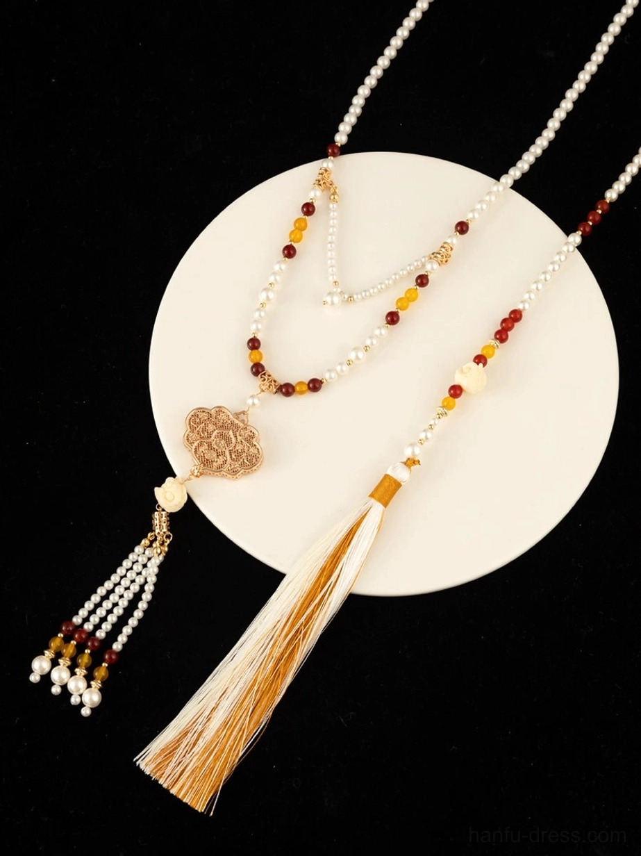 Close up of a Chinese style yingluo tassel necklace with layered beaded strands, carved bronze Ruyi charm, freshwater pearl details, and elegant silk tassel decorations