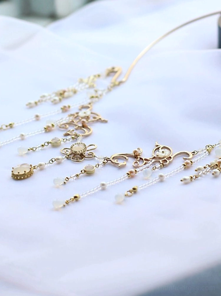 Elegant Chinese yingluo necklace photographed from an angled view with symmetrical gold chains, tiny bead details, and clear and white tassel accents