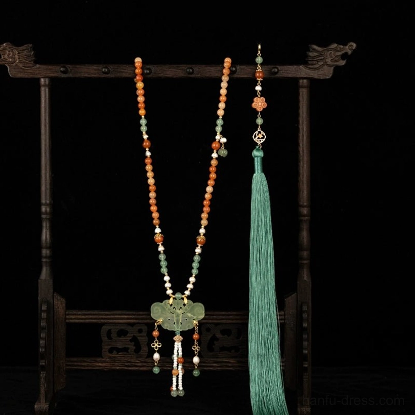 Full front view of a Chinese-style yingluo tassel necklace on a traditional dragon-head wooden jewelry stand, with warm-toned beads, green tassel details, and oriental decorative charms