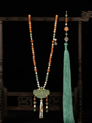 Full front view of a traditional Chinese yingluo tassel necklace on a vintage wooden jewelry stand, featuring warm-toned beads, a green ornamental pendant, and a long flowing silk tassel against a black background