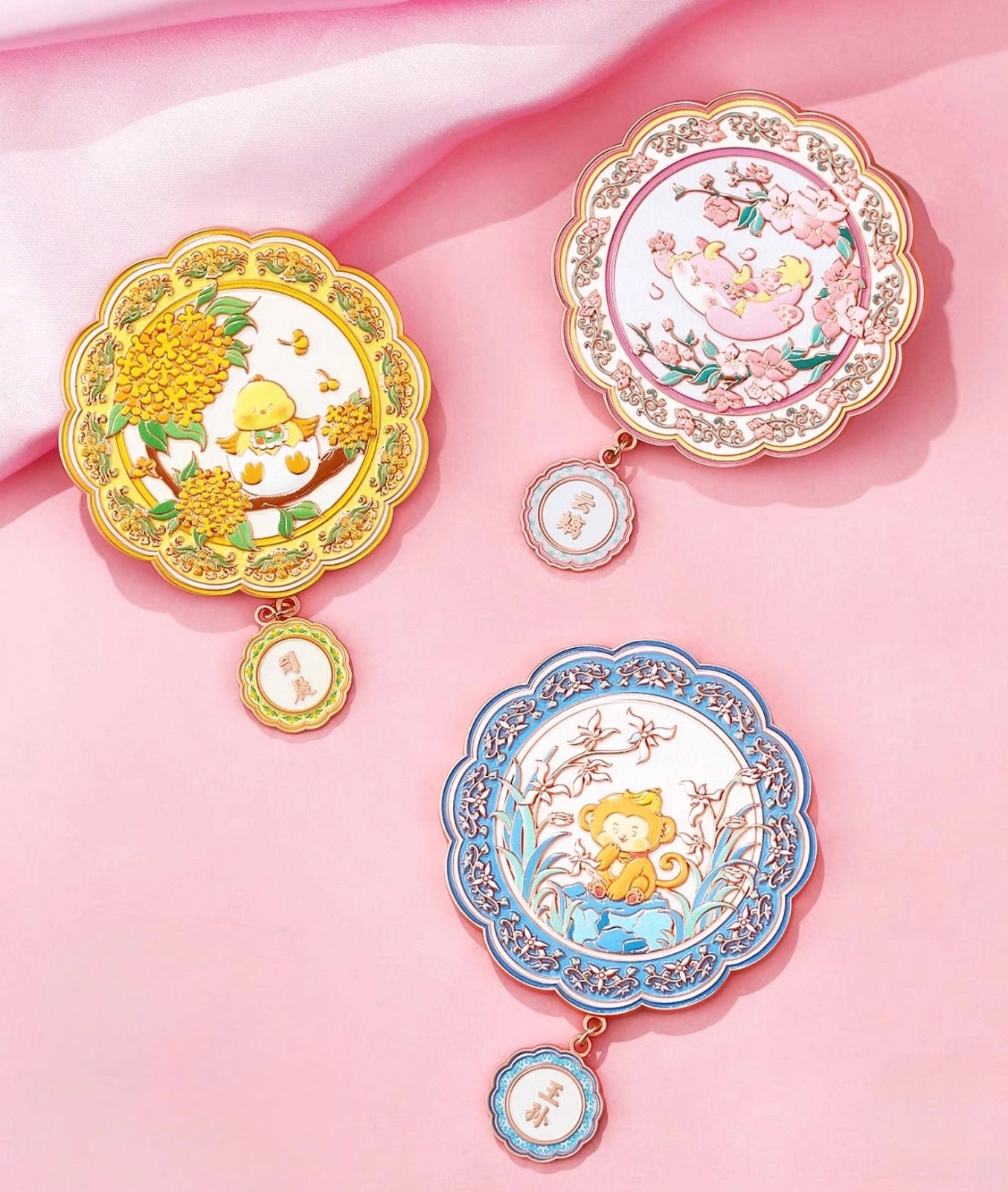 Three Chinese zodiac blessings pocket mirrors with yellow pink and blue scalloped frames on soft pink satin fabric
