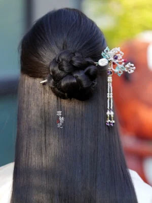 Woman wearing chrysanthemum pearl tassel Chinese hairpin on a low braided bun for an elegant Hanfu inspired hairstyle