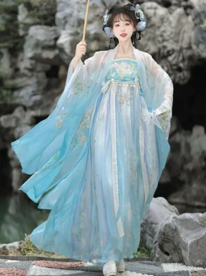 Blue Tang Dynasty style Hanfu Heziqun dress with embroidered bodice and flowing sheer wide sleeves by a waterside rock garden