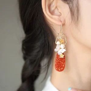 Close-up model wearing cinnabar butterfly tassel Chinese earrings showing layered red pendant, pearl-like bead, gold flower charm and white butterfly detail