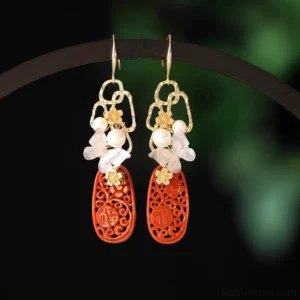 Cinnabar butterfly tassel Chinese hook earrings with red openwork pendants, pearl-like beads, gold floral charms and white butterfly details on jewelry display
