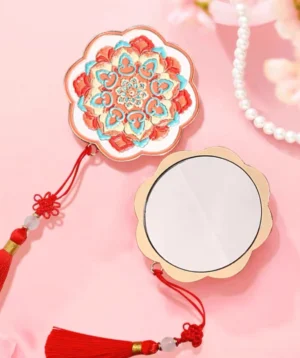 Cinnabar lotus Chinese pocket mirror shown from the front and back with scalloped flower-shaped frame, colorful embossed floral design, red Chinese knot, tassel, and jade-like bead accents