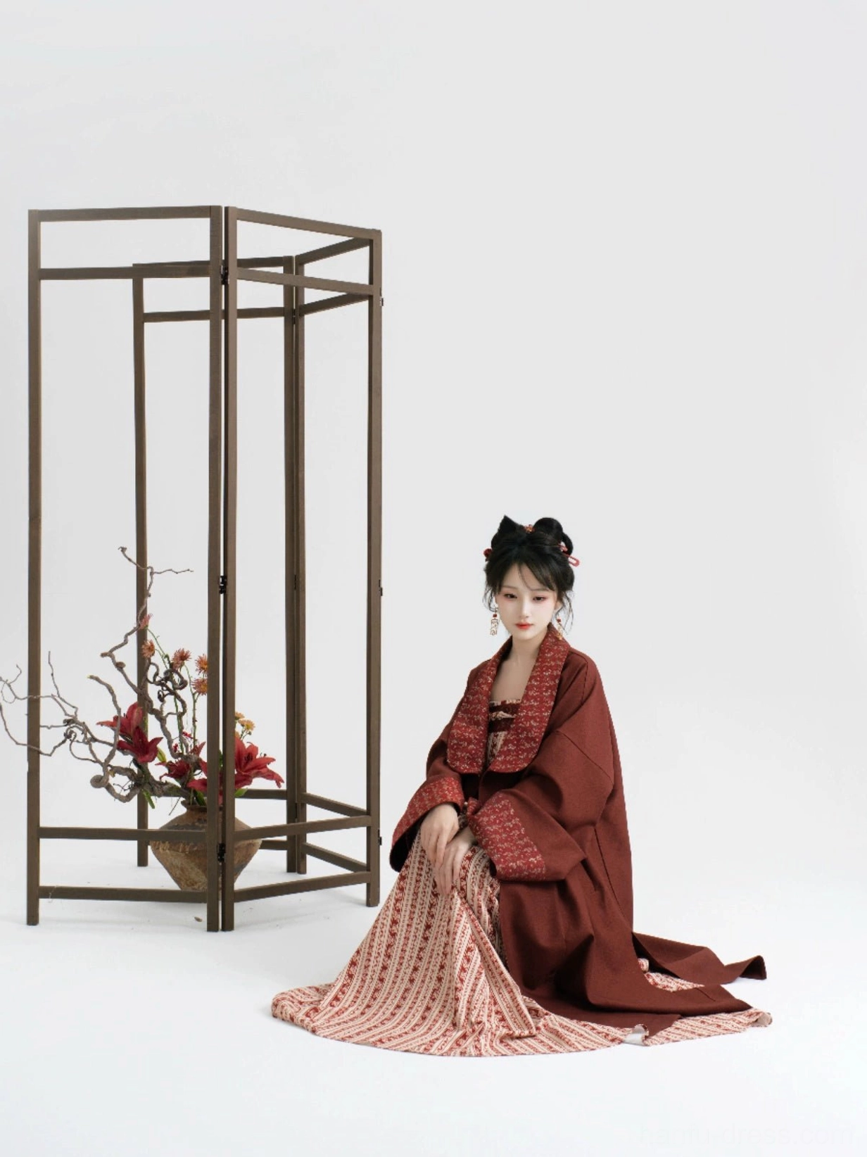 Seated model showing the flowing burgundy Hanfu coat and long striped slip dress styled as a layered outfit