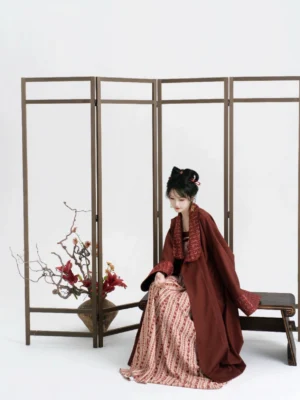 Model wearing a burgundy modern Tang Dynasty Hanfu coat over a beige and red striped slip dress in a minimalist studio
