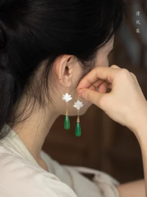 Woman wearing classic jade lotus drop Hanfu earrings with white carved lotus charms and green teardrop pendants against a soft neutral background