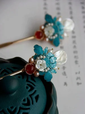 Close-up side view of a classical Chinese peony hair stick with blue floral enamel details, white shell accents, freshwater pearls, and red agate decoration