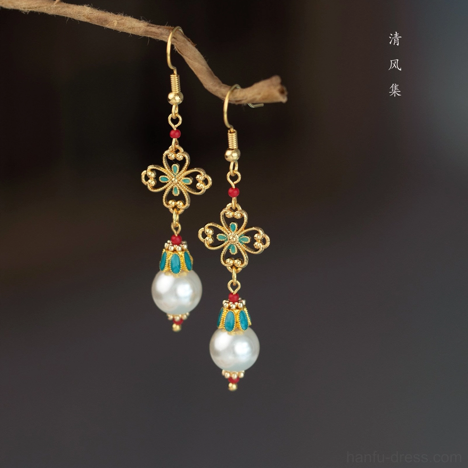 Classical Chinese antique earrings with pearl pendants gold filigree four leaf charms turquoise details and red beads displayed from a low angle