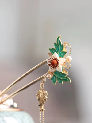 Close-up classical Chinese hair stick featuring a white flower red center green enamel foliage pearl accents and elegant maple leaf pendant