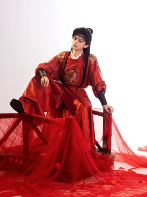 Male model seated in a crimson Tang Dynasty round-collar hanfu robe with golden dragon chest embroidery in a red draped studio setting