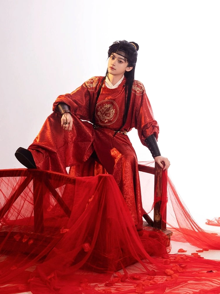 Male model seated in a crimson Tang Dynasty round-collar hanfu robe with golden dragon chest embroidery in a red draped studio setting