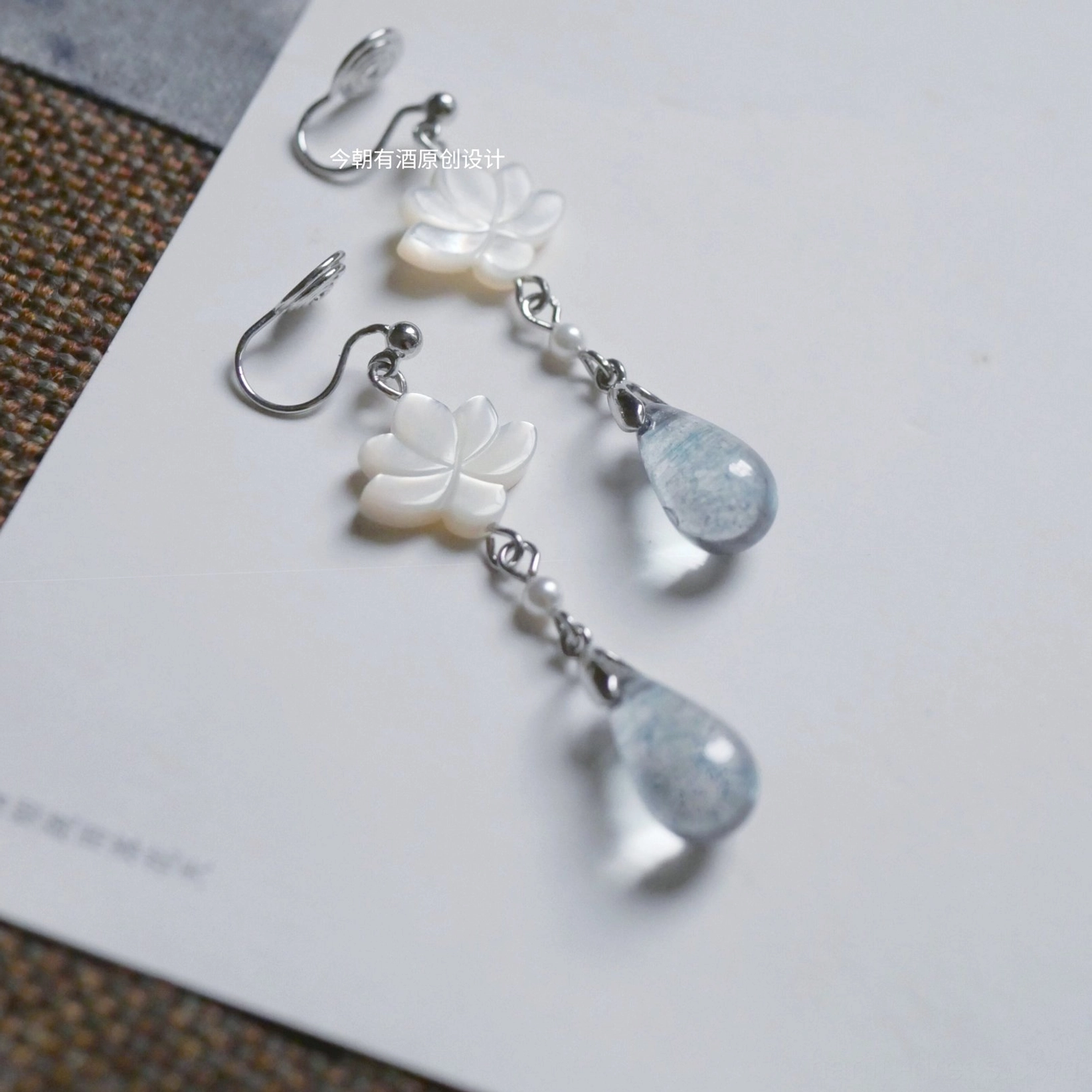 Lotus drop Hanfu earrings shown in hook and comfort clip-on styles with white floral carvings faux pearls and smoky blue glass pendants