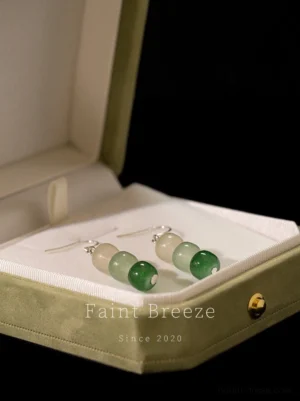 Clear Spring on the Stone Chinese earrings displayed inside a green velvet jewelry box, featuring three graduated green barrel beads and shiny silver-tone earring hardware