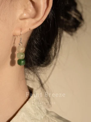 Close-up side view of Clear Spring on the Stone Hanfu dangle earrings worn with a light traditional Chinese-style top, showing three graduated ivory beige and green beads with polished silver hardware