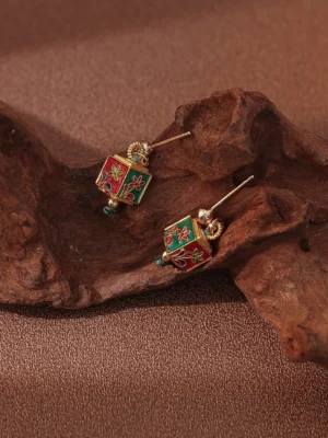 Pair of cloisonne-inspired floral cube drop Chinese earrings with red green enamel-style patterns gold-tone frames and blue crystal accents on a rustic background