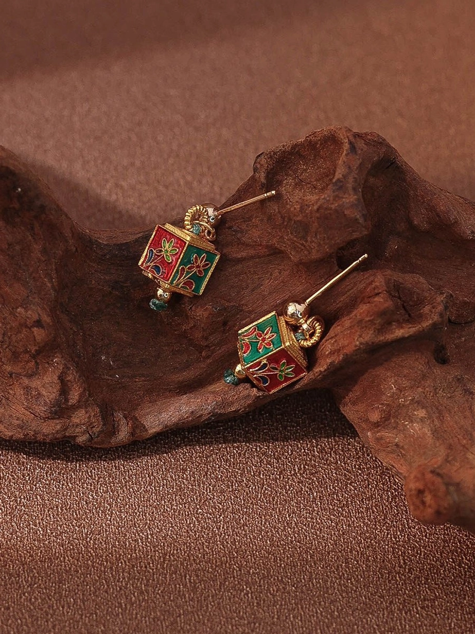 Pair of cloisonne-inspired floral cube drop Chinese earrings with red green enamel-style patterns gold-tone frames and blue crystal accents on a rustic background