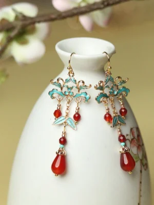 Cloisonne red agate drop earrings hanging from a white porcelain vase with blue floral enamel motifs and gold tone hardware