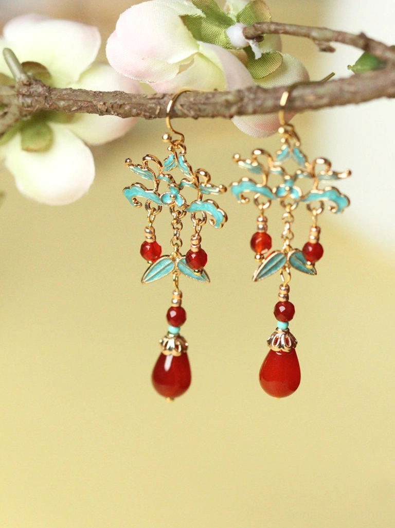 Front view of paired cloisonne style red agate teardrop earrings with gold tone floral details on tree branches