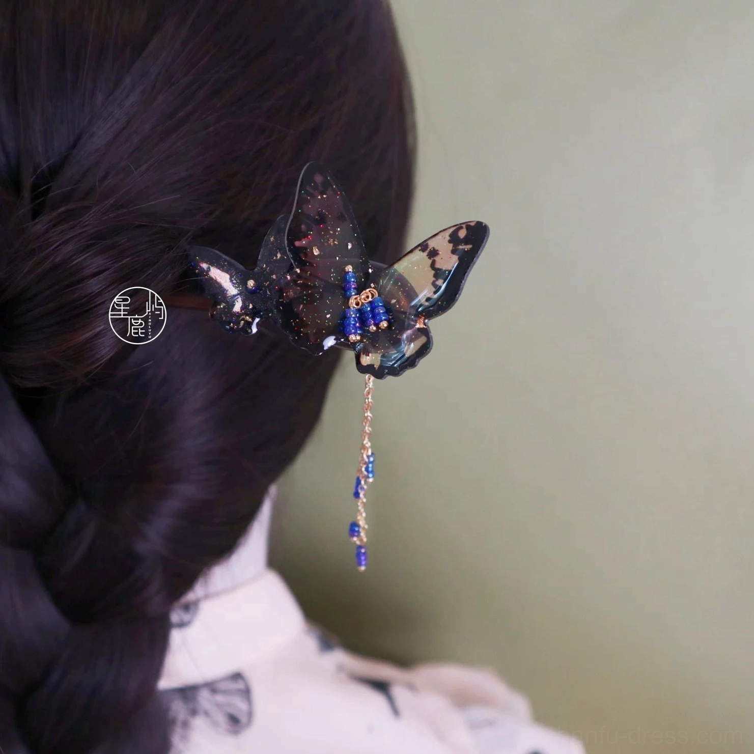 Close-up butterfly Chinese hair stick secured in an elegant updo showing glitter inlay and blue gold hanging tassel details