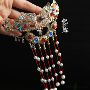 Close-up view of a traditional Chinese butterfly back hair pin with hollow filigree ornament gemstone accents and layered red tassel chains