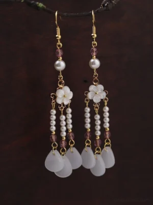 Close-up view of traditional Chinese earrings showing layered white flower charms pearl strands purple beads and gold-tone details
