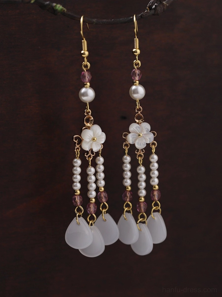 Close-up view of traditional Chinese earrings showing layered white flower charms pearl strands purple beads and gold-tone details