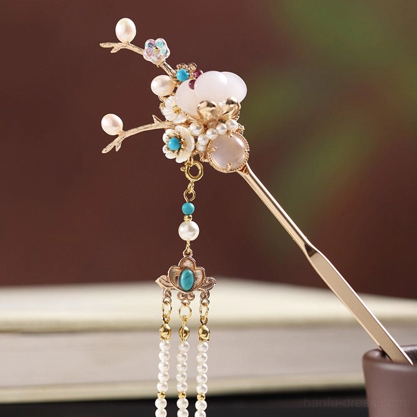 Close-up of an exquisite Chinese hair stick with a golden branch top, milky white center stone, turquoise-toned accents, layered pearl tassels, and carved pendant