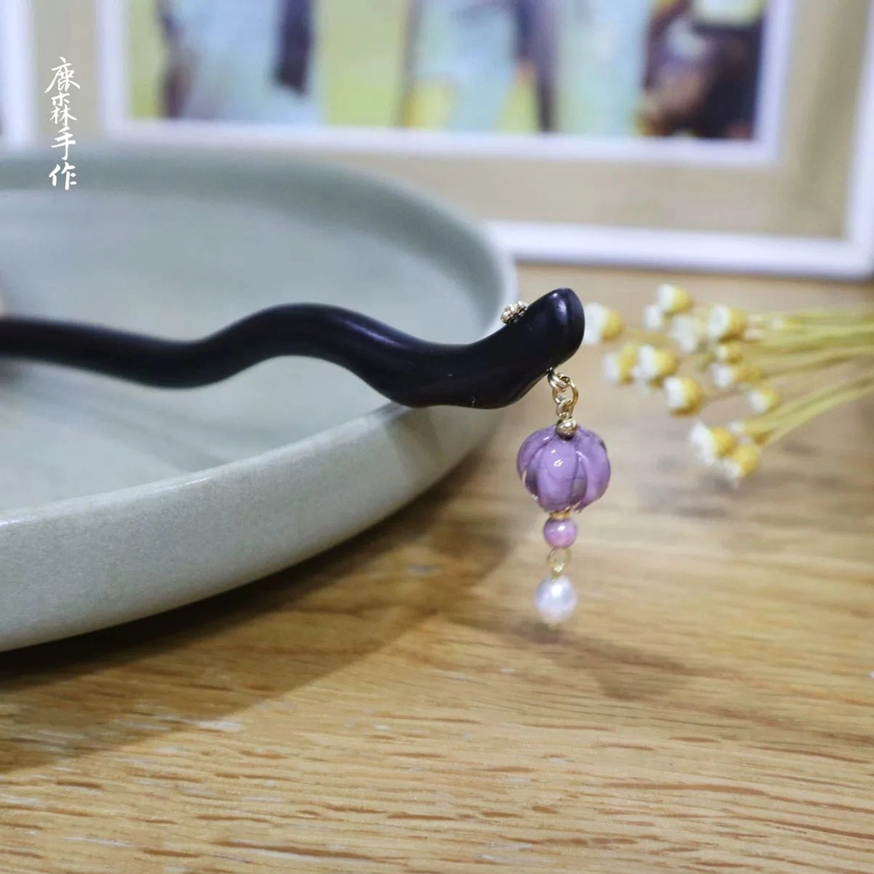 Close-up side view of a handmade ebony Hanfu hair stick showing the wavy wooden shaft, purple decorative bead, pink bead, white pearl, and dangling pendant