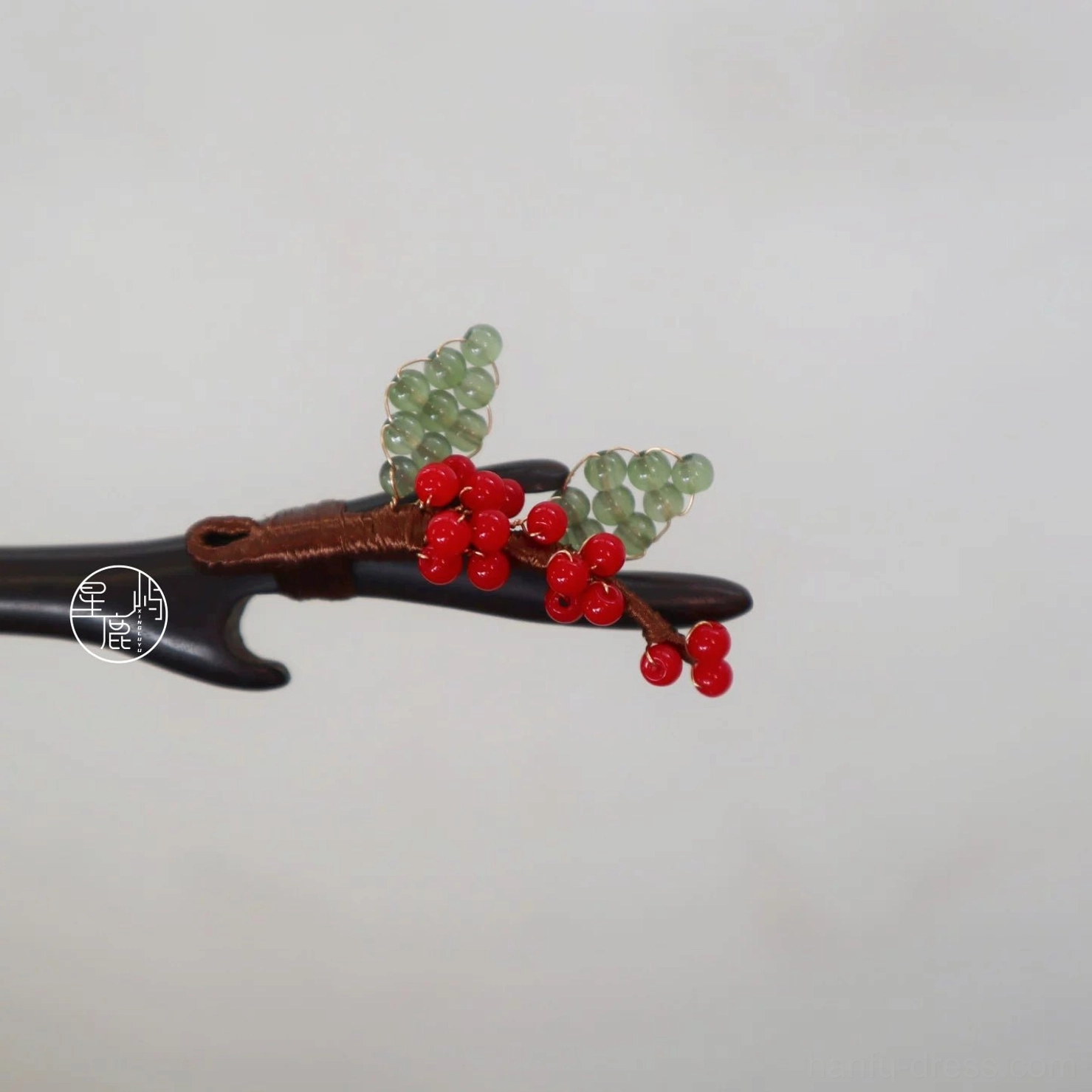 Close-up of a handmade Chinese hair stick showing natural branch-style wood, red berry bead clusters, green leaf accents, and detailed brown thread wrapping