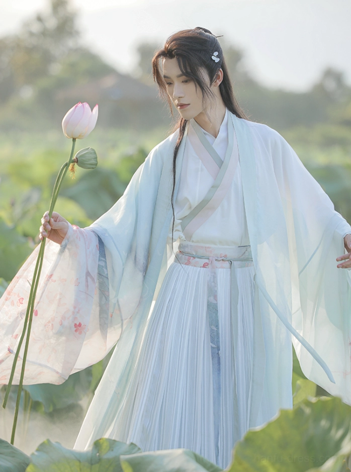 Three-quarter view of the Cloud Pavilion hanfu for men showing the light blue pleated ruqun skirt, sheer gradient outer coat, wide sleeves, and delicate floral embroidery beside blooming lotus flowers
