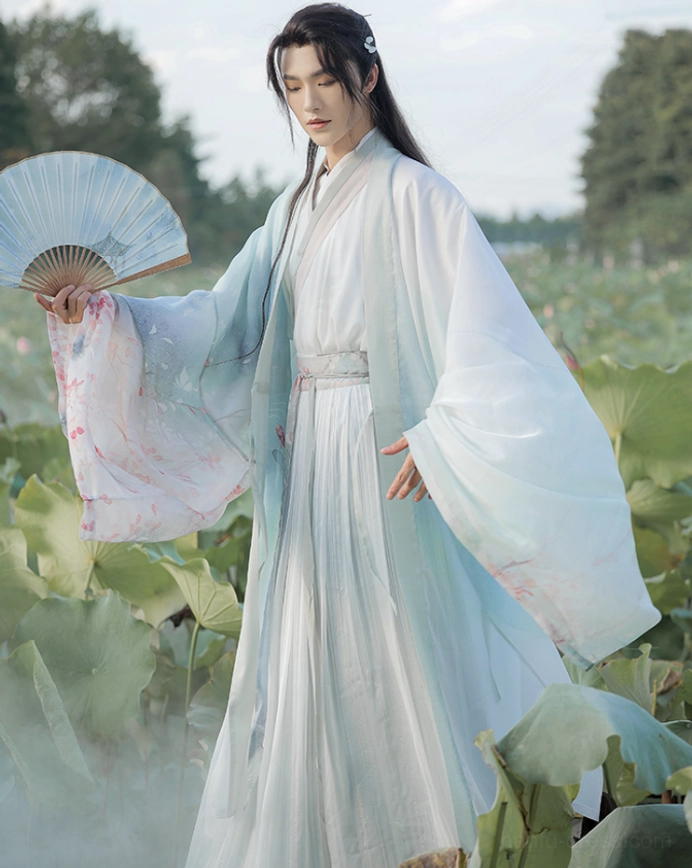 Full-body view of a male model wearing the Cloud Pavilion Wei Jin wuxia hanfu with a light cyan gradient outer robe, ivory cross-collar top, embroidered sleeves, and matching waist sash beside a lotus pond