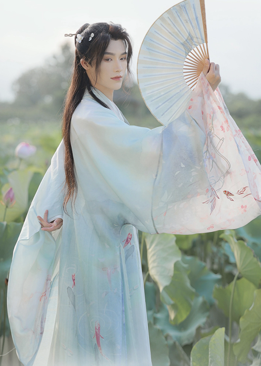 Back three-quarter view of the Cloud Pavilion Wei Jin hanfu showing the flowing outer robe train, wide sleeves, loose silhouette, hairpins, and folding fan held behind the back