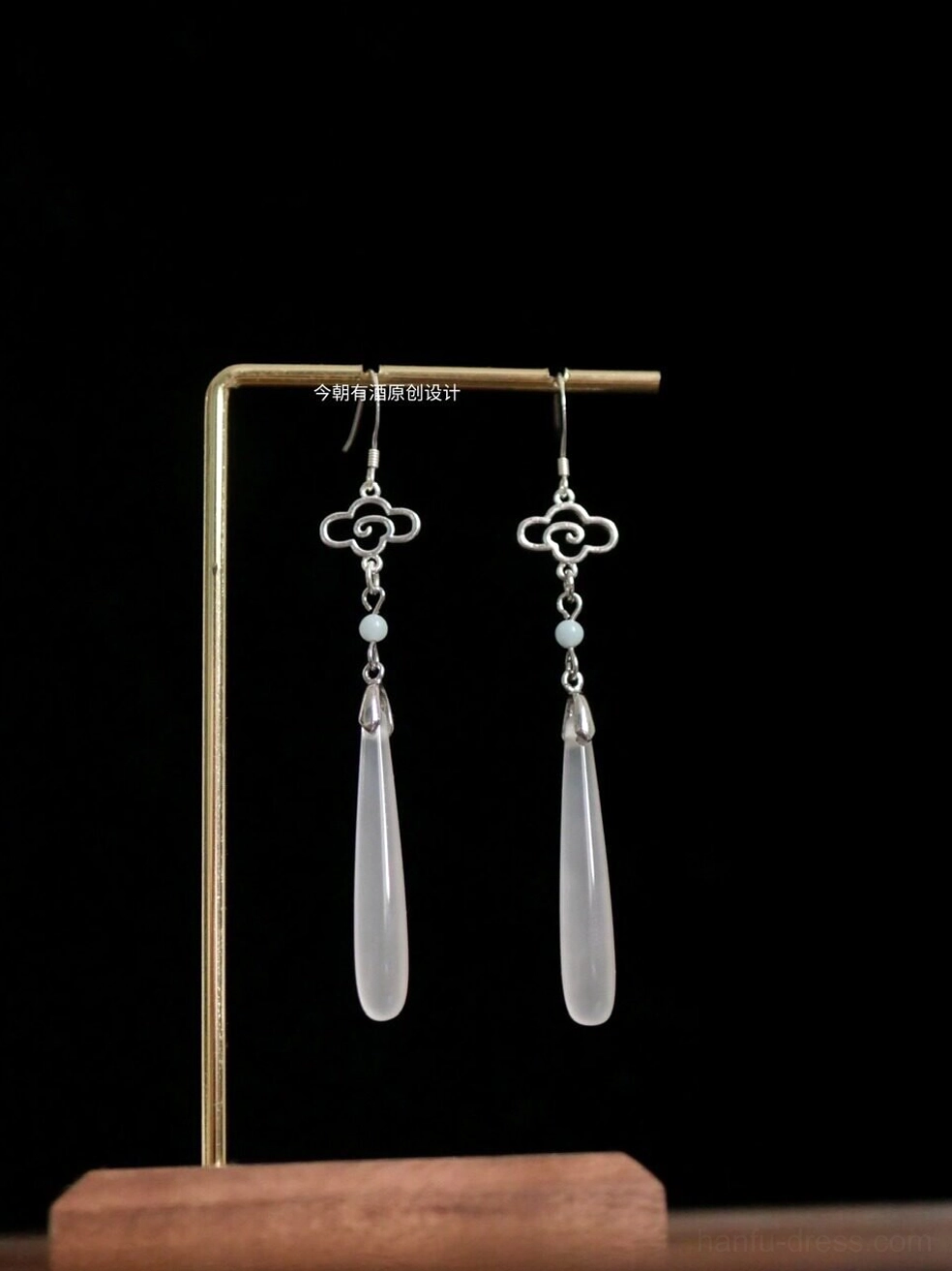 Traditional Chinese Hanfu cloud motif drop earrings with silver-tone openwork cloud hook, light blue bead, and long white agate pendant displayed on a brass jewelry stand