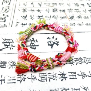Colorful handwoven Chinese bracelet with textured knotwork and flowing tassel placed on a Luo Shen Fu ancient Chinese calligraphy scroll