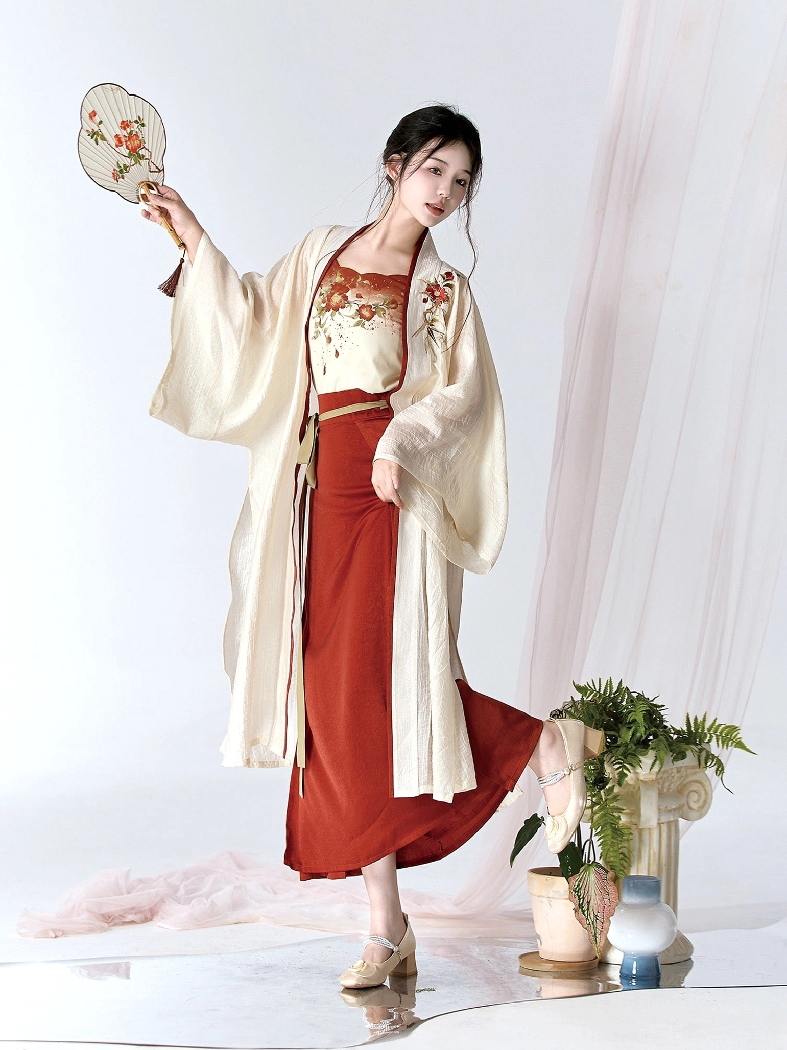 Three-quarter side view of a complete modern Hanfu set with camellia camisole embroidery, cream cardigan, burgundy skirt, and vintage heels