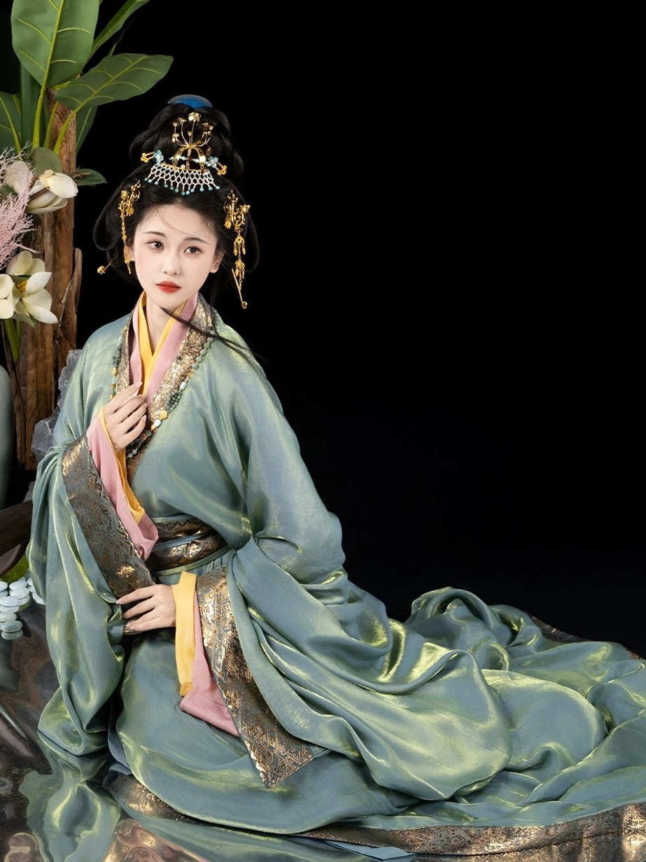 Seated model wearing a complete straight hem Han Dynasty hanfu set with cyan blue outer robe, gold collar trim, pink and yellow layers, wide sleeves, and waist belt