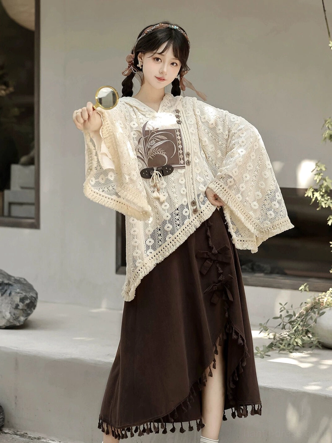 Contemporary everyday Hanfu outfit with beige asymmetrical lace hooded top and brown midi skirt shown on a model holding a small round mirror outdoors
