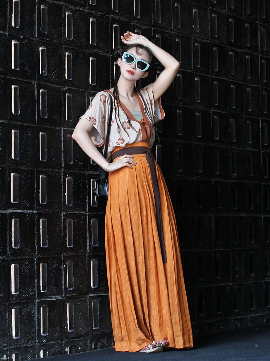 Contemporary Tang-style hanfu outfit with orange pleated skirt, floral top, brown waist sash, and shoulder bag